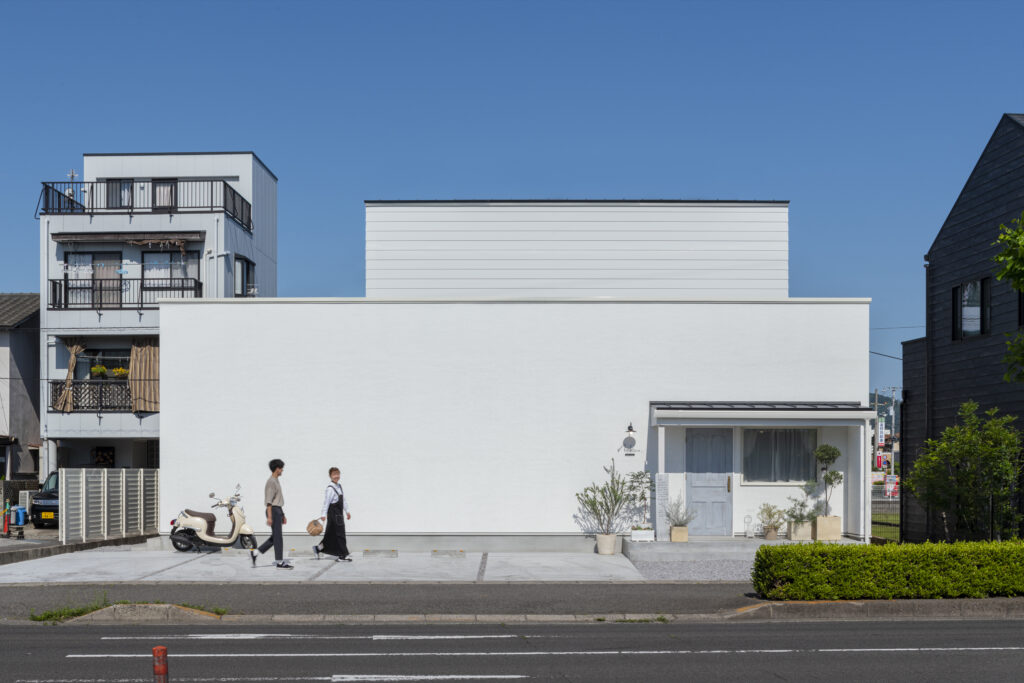 友人をもてなす横長の白い店舗併用住宅の外観